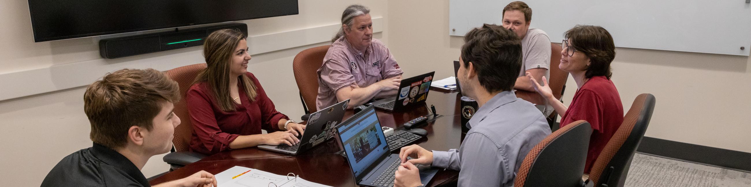 Six employees working together on their laptops in a conference room.