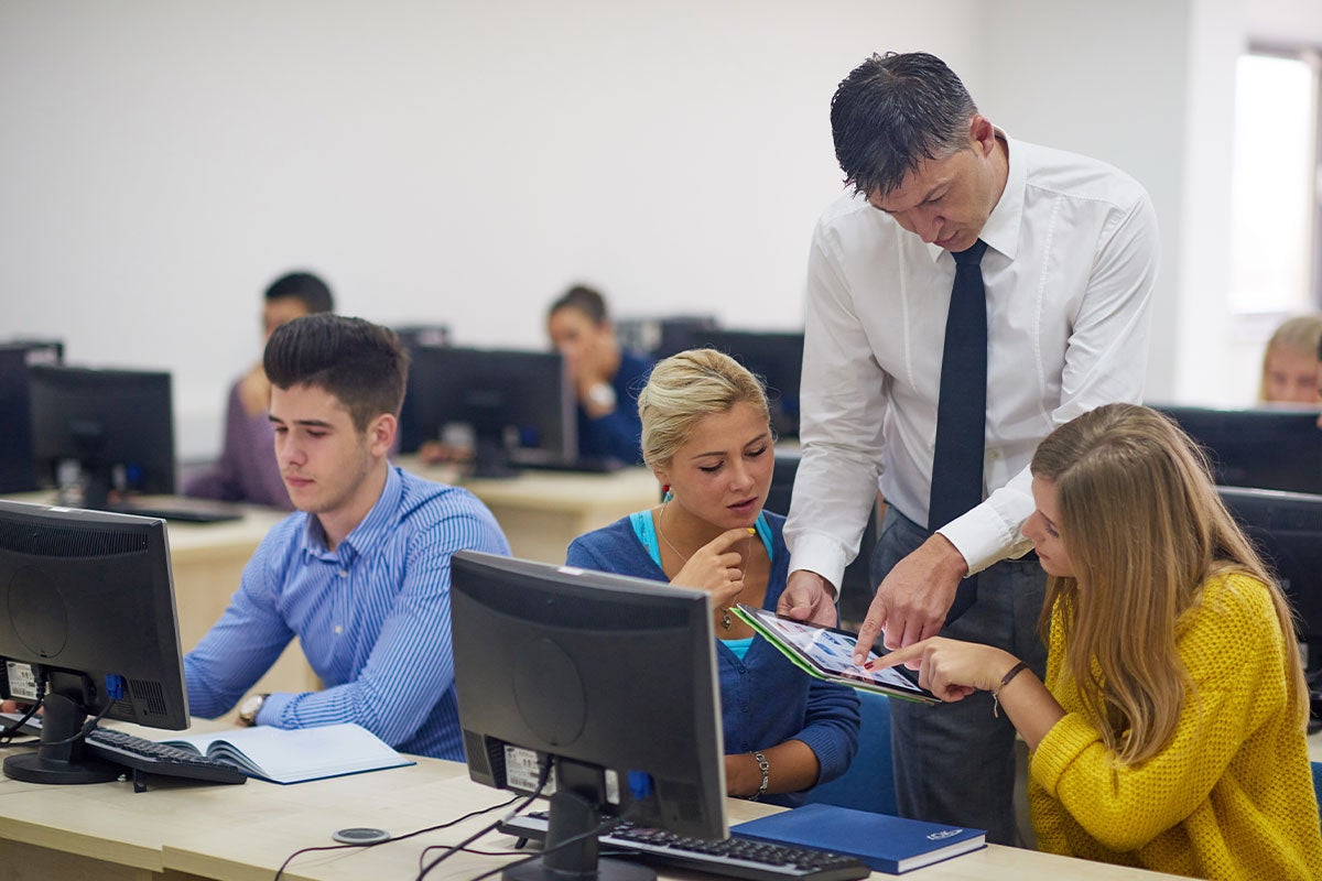 A teacher working with three students in a computer lab.